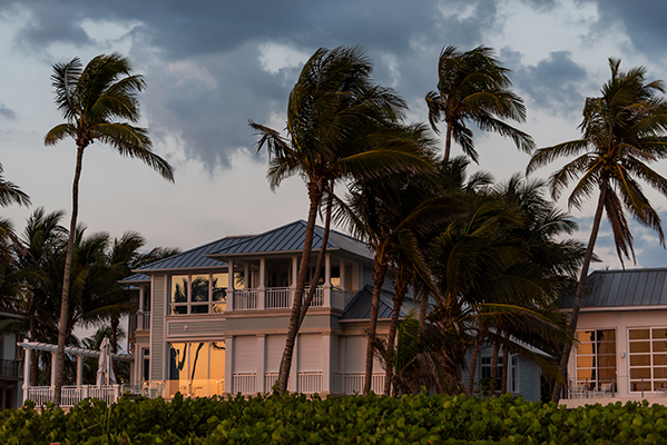 The image depicts a beachfront scene at sunset with palm trees, a house with a white exterior, and a cloudy sky.