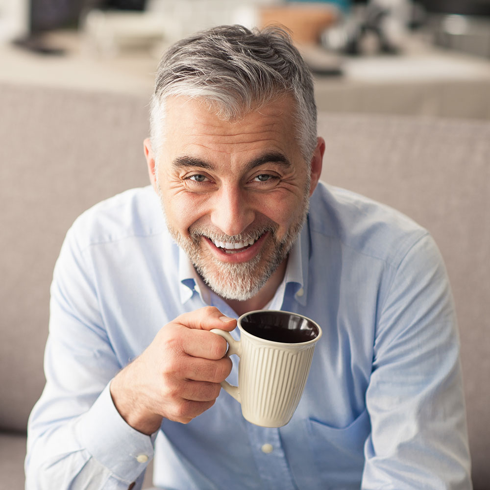 A smiling man in a blue shirt holding a coffee mug.